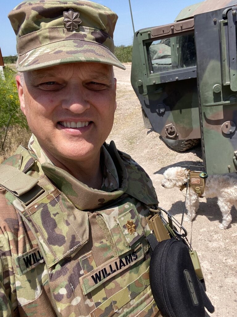 A man in camouflage standing next to a truck.